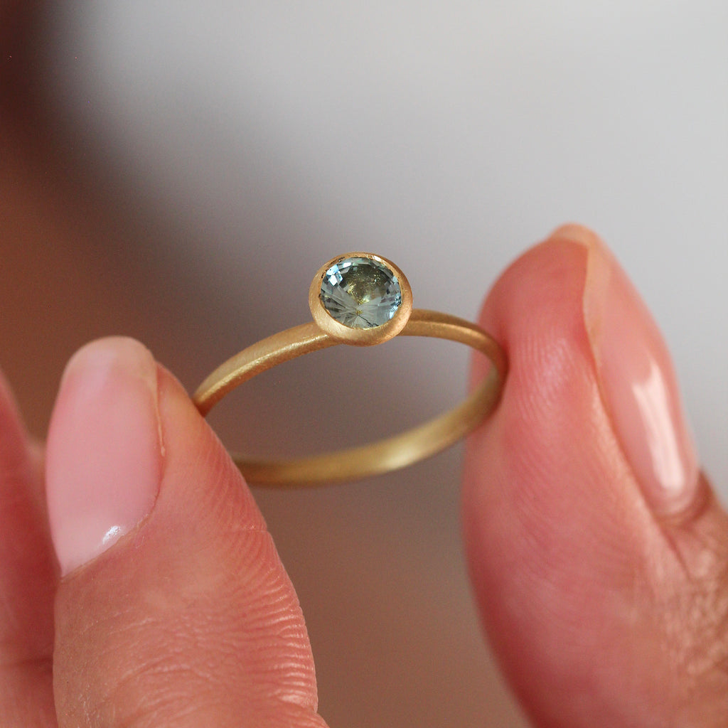 An 18ct yellow gold engagement ring with a bezel setting featuring a sea blue Sapphire by contemporary jewellery designer, Sarah Straussberg