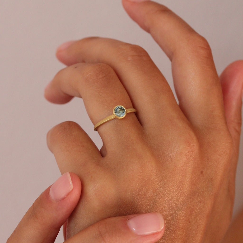 An 18ct yellow gold engagement ring with a bezel setting featuring a sea blue Sapphire by contemporary jewellery designer, Sarah Straussberg