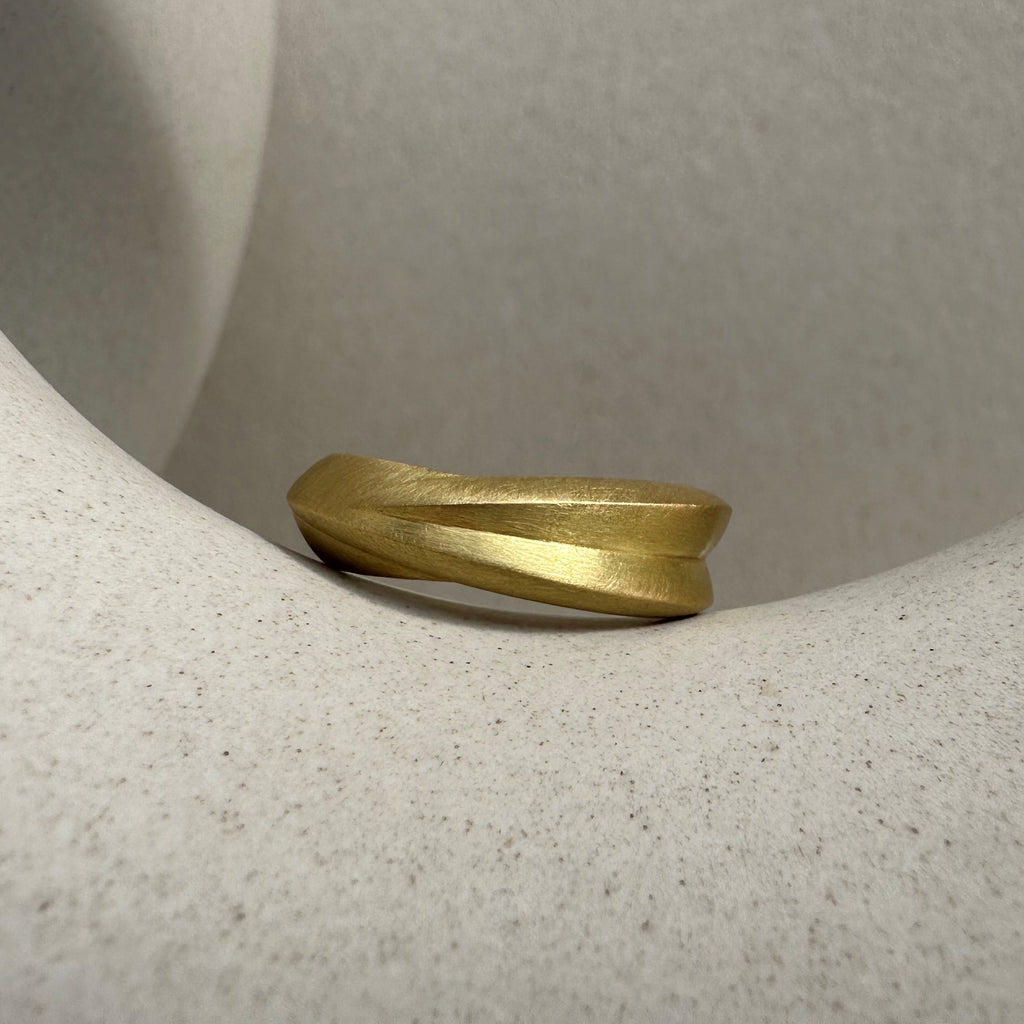 A chunky 18ct yellow gold ring with a matte finish, displayed against a beige background. By contemporary jewellery designer, Sarah Straussberg