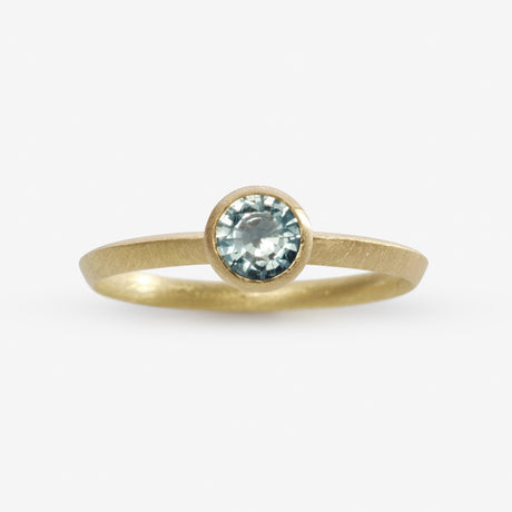 An 18ct yellow gold engagement ring with a bezel setting featuring a sea blue Sapphire by contemporary jewellery designer, Sarah Straussberg