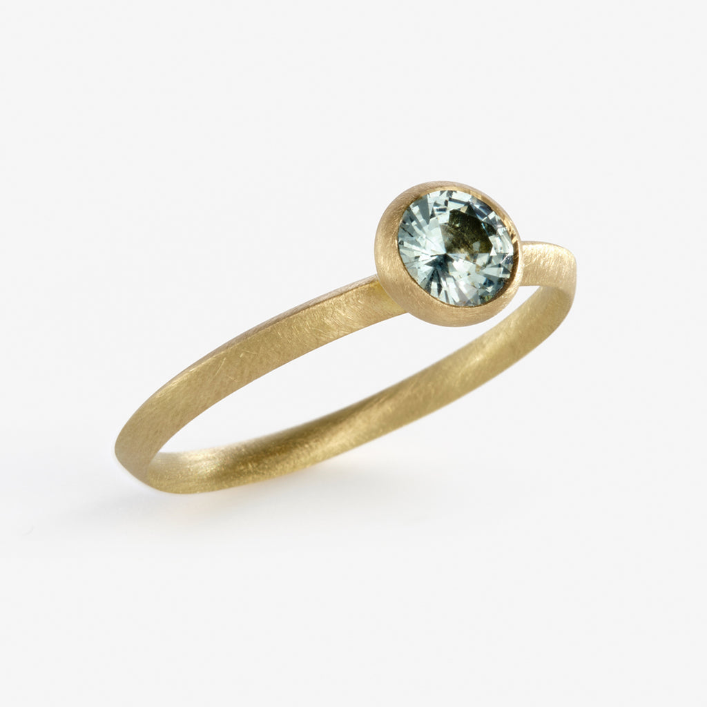 An 18ct yellow gold engagement ring with a bezel setting featuring a sea blue Sapphire by contemporary jewellery designer, Sarah Straussberg