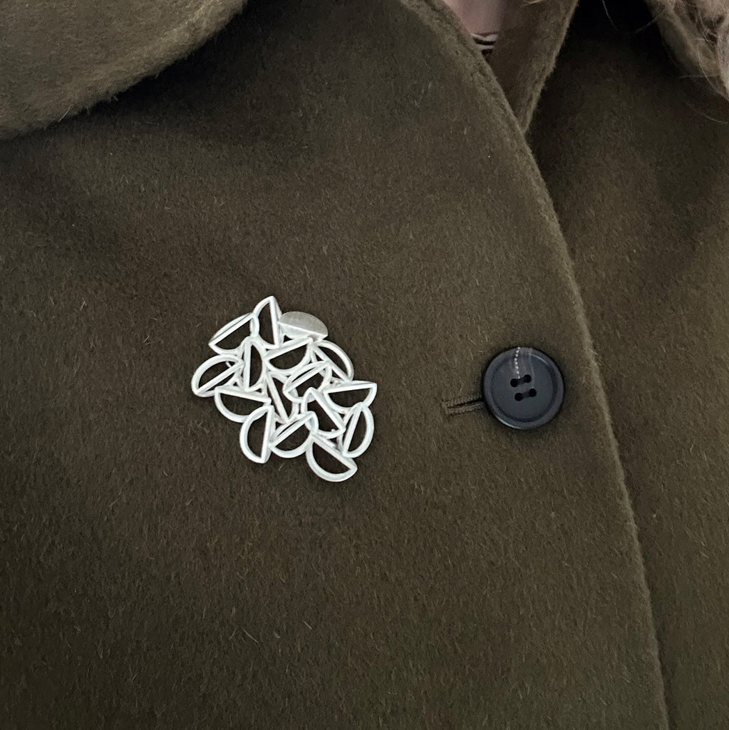 Silver geometric brooch shown on khaki coat from Sarah Straussberg