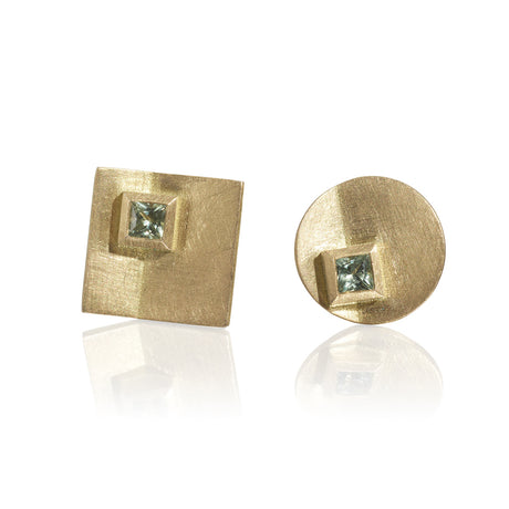 A pair of asymmetric sapphire earrings with a matte finish in yellow gold, featuring princess cut green sapphires by contemporary jewellery designer, Sarah Straussberg