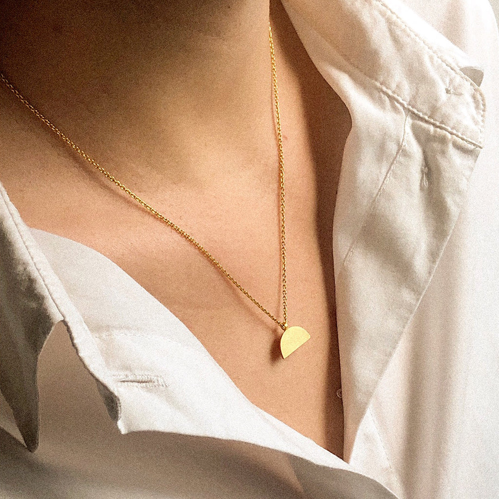 A gold pendant necklace with a brushed finish. The pendant has a semi-circular shape, by contemporary jewellery designer, Sarah Straussberg